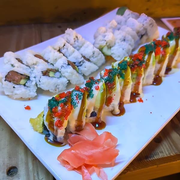 A white plate of Royal Thai and Sushi's colorful sushi rolls with ginger on a wooden table.