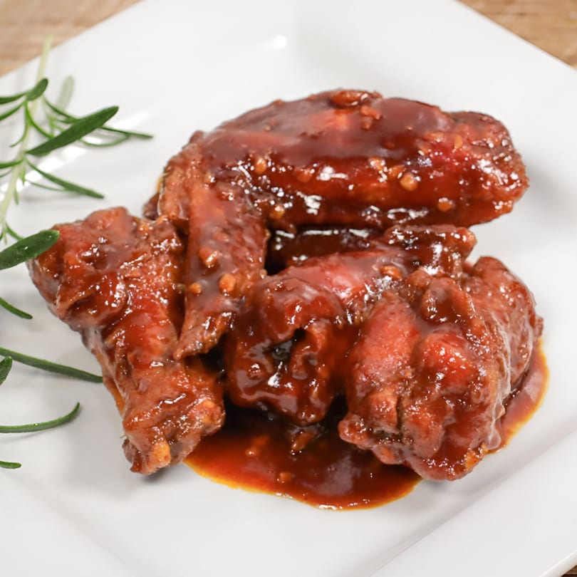 Close-up of Royal Thai and Sushi's sticky, sweet Thai chicken wings with rosemary garnish on a white plate.