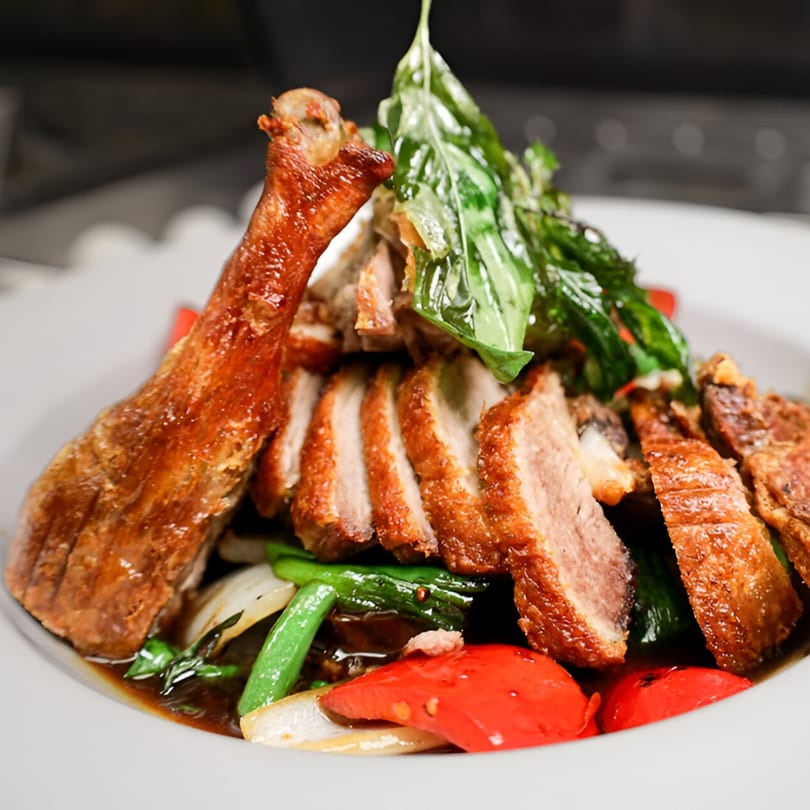 Crispy duck leg and sliced duck breast with basil, red peppers, and green beans in sauce.