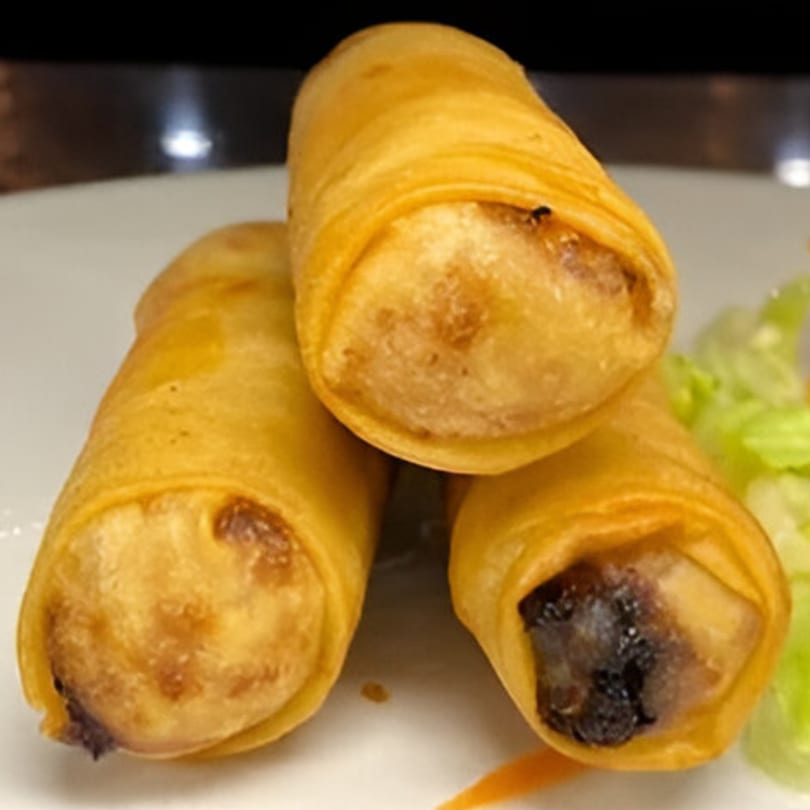 Three crispy golden Thai spring rolls on a white plate with a side of lettuce.